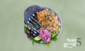 A bowl with rice, black beans, lettuce, shredded carrots, pickled onions, lime wedges, a blue corn tortilla, and white sauce drizzle on a light green background with 